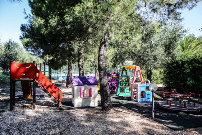 Parco giochi con scivoli colorati tra alberi e ombre.