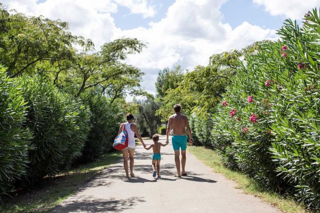 Famiglia cammina su un sentiero tra alberi e fiori.