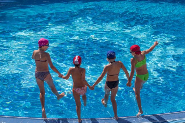 Quattro bambini si tuffano in una piscina tenendosi per mano.
