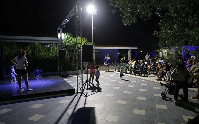 Spettacolo serale all'aperto con pubblico seduto.
