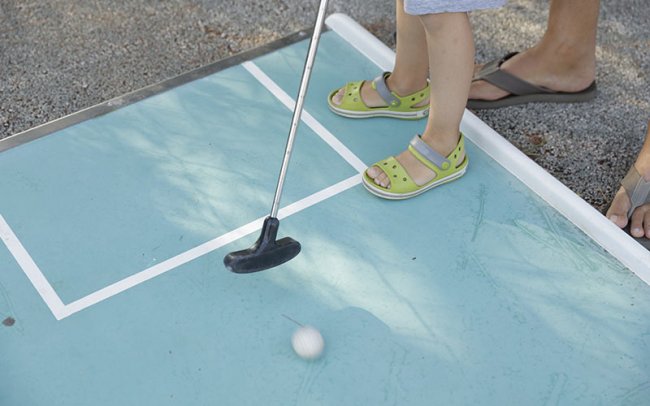 Piedi di bambino e adulto durante il mini golf.
