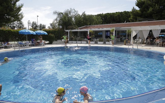 Piscina rotonda con bagnanti e ombrelloni blu.