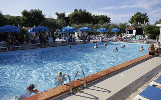 Piscina lunga con bagnanti e sdraio.