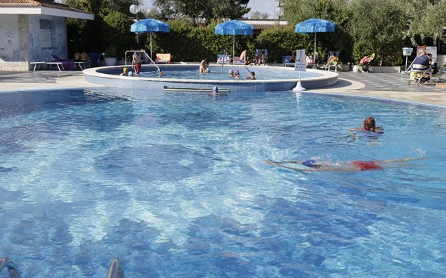 Piscina all'aperto con bagnanti e ombrelloni.