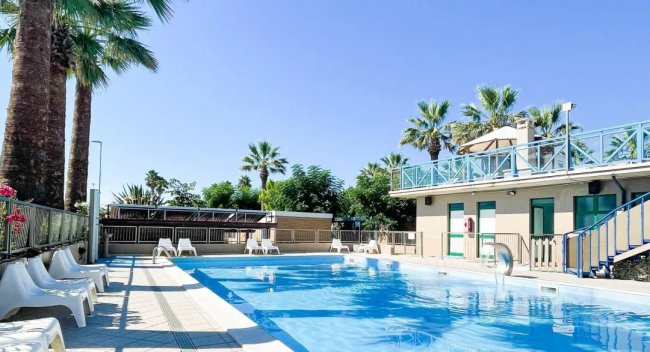 Piscina all'aperto con lettini e palme.