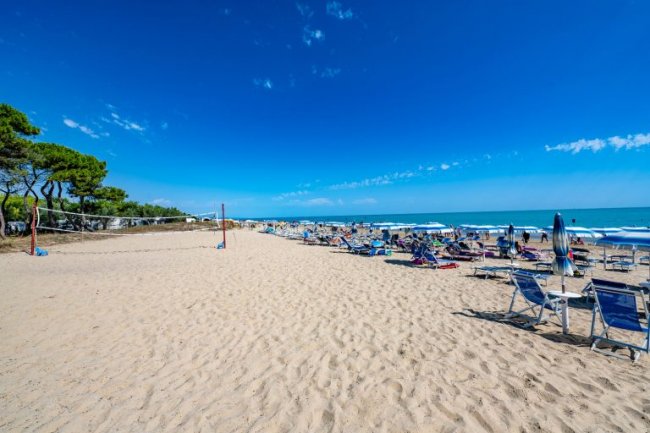 Spiaggia con ombrelloni e lettini sotto un cielo azzurro.