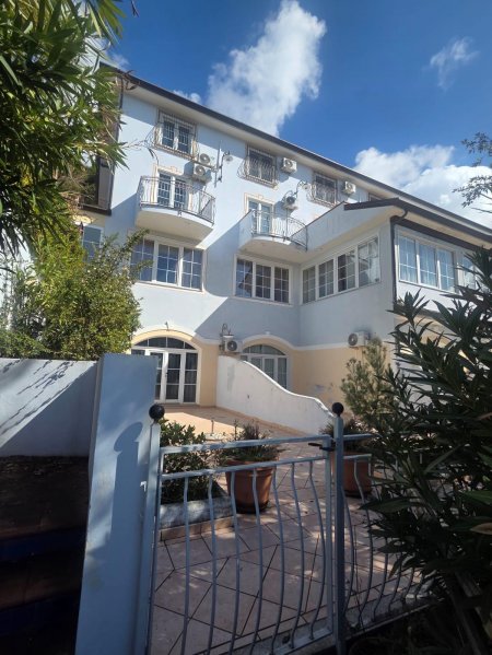 Facciata di un edificio a tre piani con balconi, finestre ampie e circondato da piante.