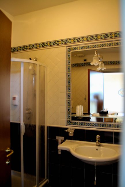 Bagno con doccia, lavabo e specchio incorniciato da piastrelle decorative.