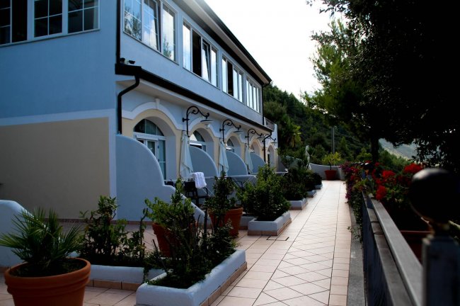 Edificio azzurro con portico e giardino fiorito lungo un corridoio esterno.