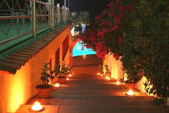 Scalini illuminati da candele accanto a piante in vaso, conducono a una piscina.