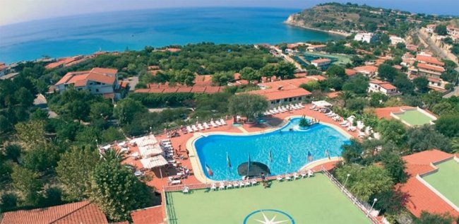 Vista aerea di un complesso turistico con piscina e mare sullo sfondo.