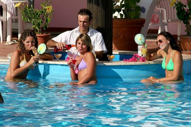 Persone che bevono cocktail in una piscina con bar acquatico.
