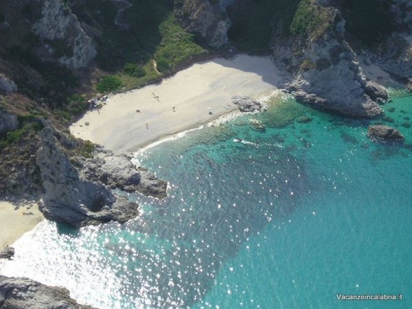 Spiaggia di sabbia bianca e acqua cristallina circondata da scogliere.