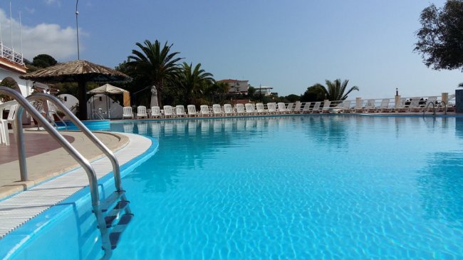 Piscina con sedie a sdraio bianche e palme sullo sfondo.