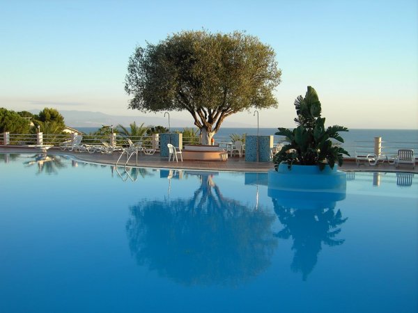 Una piscina riflette un albero, con sedie e vista mare.