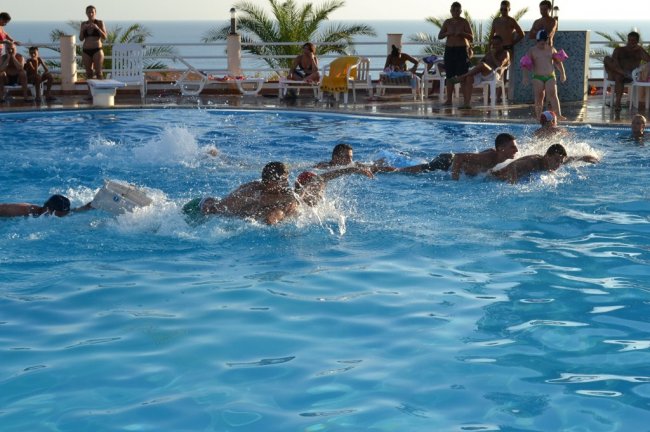 Persone che nuotano in una piscina, con spettatori sullo sfondo.