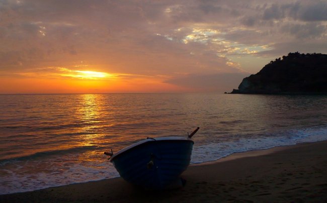 Barca sulla spiaggia al tramonto, con cielo arancione e mare calmo.