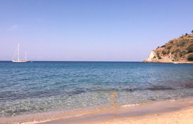 Spiaggia sabbiosa con mare blu e barca a vela.