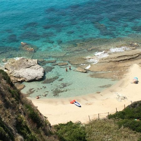 Piccola caletta circondata da rocce e acqua turchese. Persone sulla sabbia e un ombrellone colorato.