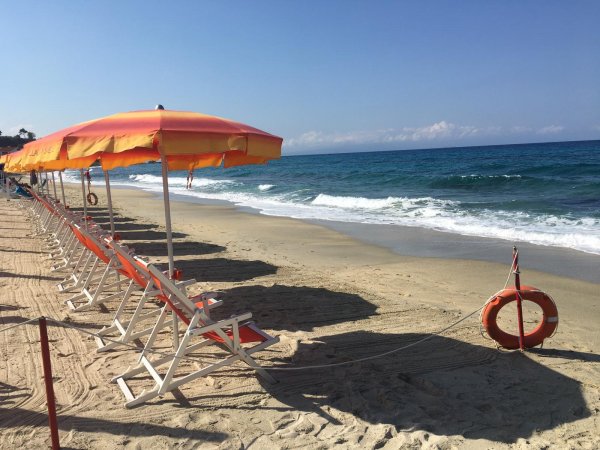 Spiaggia con sedie a sdraio e ombrelloni arancioni, mare mosso e cielo sereno.