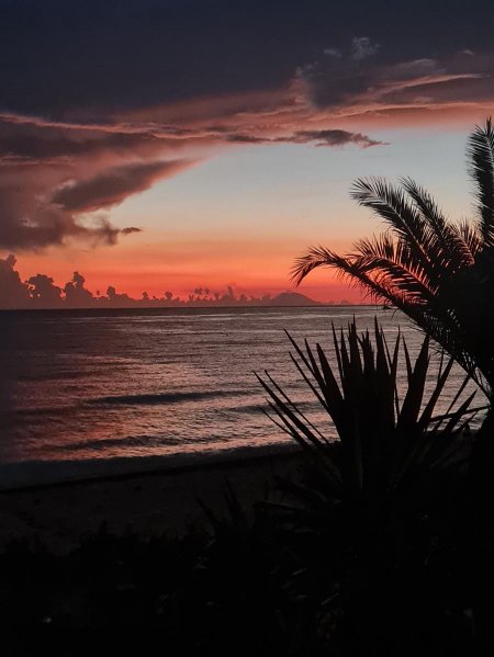 Un tramonto con cielo rosso-arancio e nuvole sopra il mare calmo in primo piano.