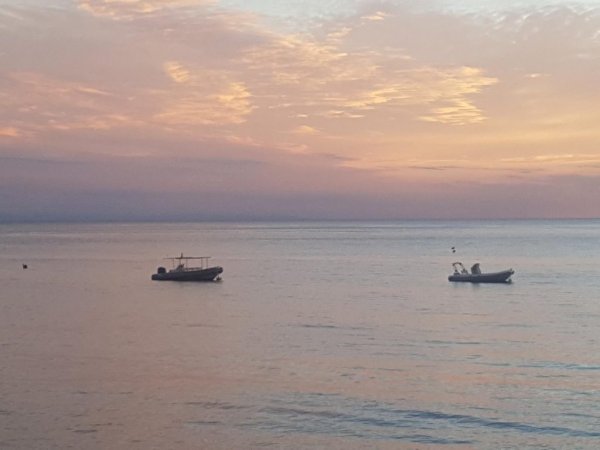 Due barche galleggiano sul mare al tramonto, sotto un cielo dai colori pastello.