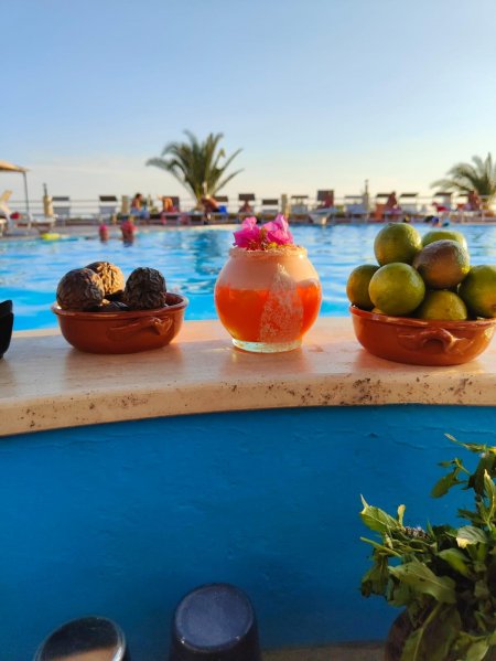Un drink arancione con fiori tra ciotole di fichi secchi e lime, vicino a una piscina.
