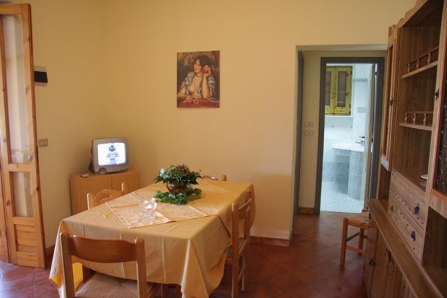 Sala da pranzo con tavolo apparecchiato, TV su mobile e porta verso il bagno.