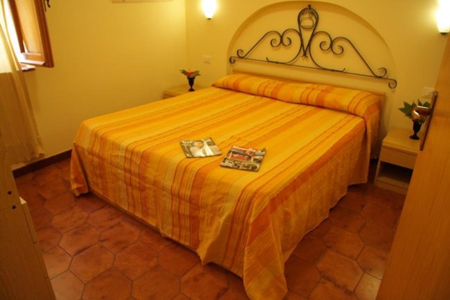 Letto matrimoniale con copriletto a righe arancioni, affiancato da due comodini.