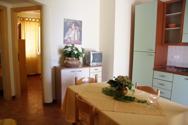 Interno di una cucina luminosa con tavolo apparecchiato, credenza e televisore.