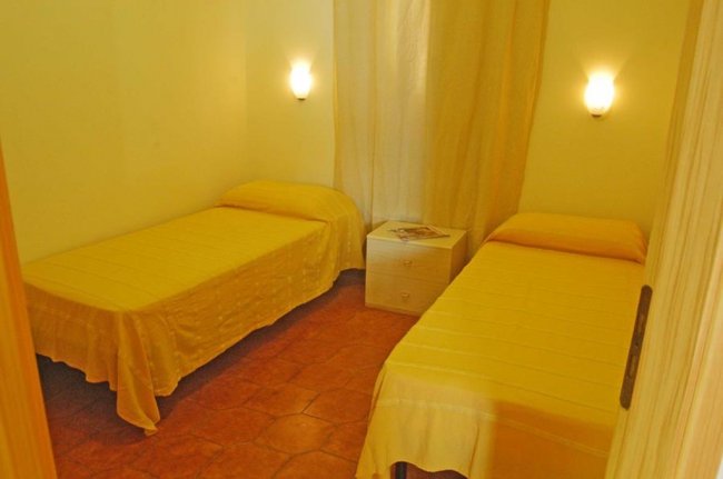 Camera con due letti singoli e pareti gialle, illuminata da due applique.
