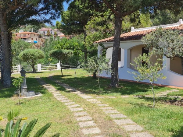 Sentiero in pietra, giardino alberato e casa bianca con tetto in tegole.