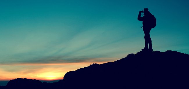 Persona su collina al tramonto con binocolo.