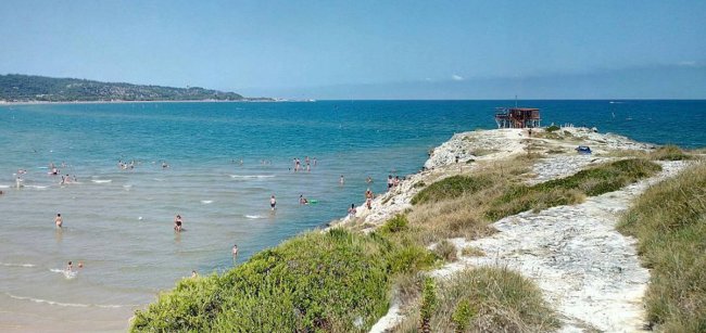 Spiaggia con bagnanti e promontorio erboso.