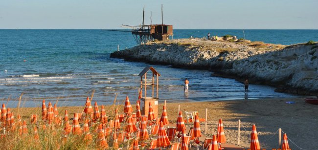 Spiaggia con ombrelloni e struttura in legno su roccia.