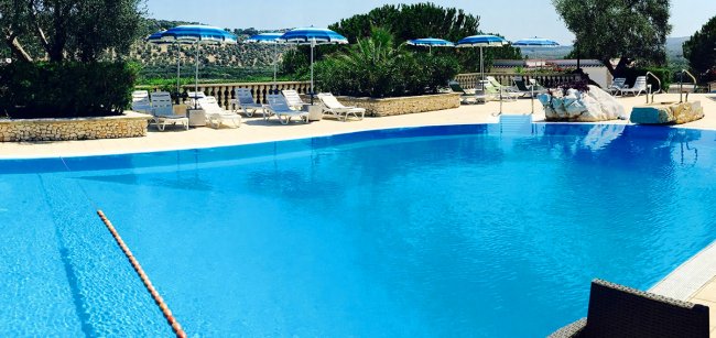 Piscina con vista su colline e lettini bianchi.