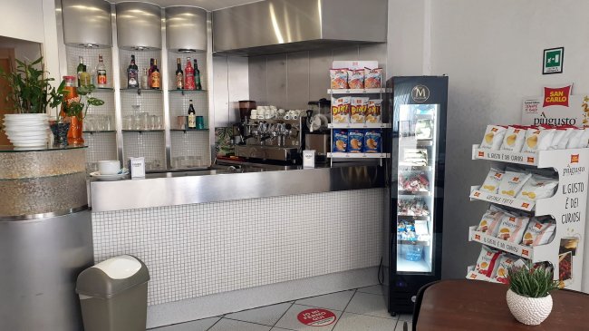 Banco di un bar moderno con scaffali di bibite, macchinetta del caffè e frigorifero per snack.